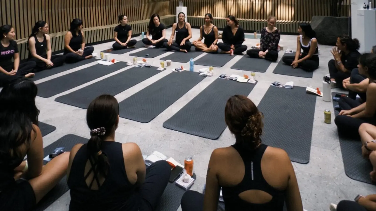 Clase grupal de yoga: alumnas sentadas en sus mats escuchando a la profesora