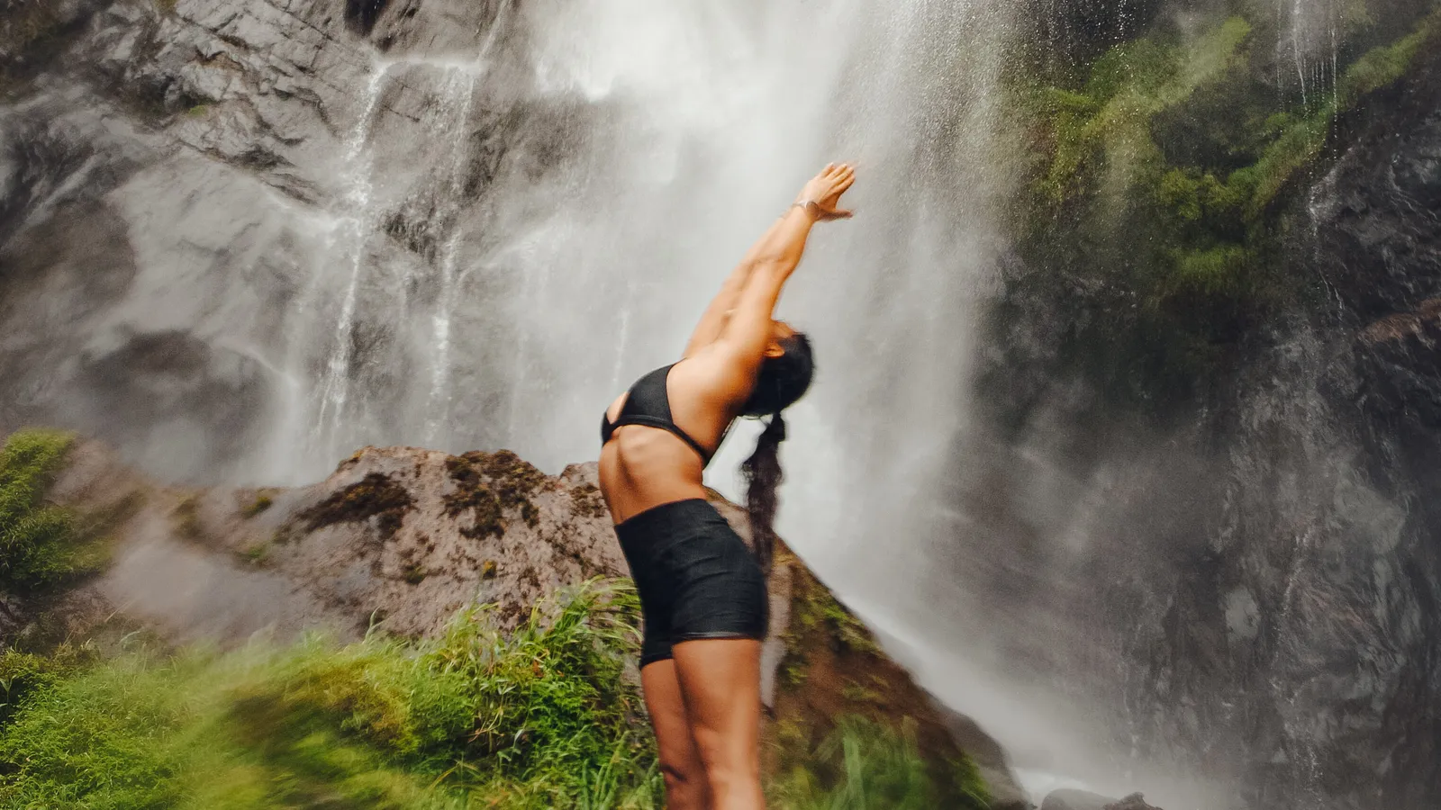 Andreina en una postura de apertura frente a una catarata en la selva de Cusco